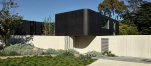 A modern black metal exterior residence with green landscaping and a white brick base.