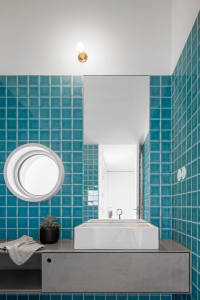 A modern bathroom featuring teal ceramic tiles, a circular window, and a white floating vanity.