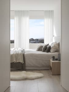 A modern minimalist bedroom with a white bed, white curtains, and wooden floor.