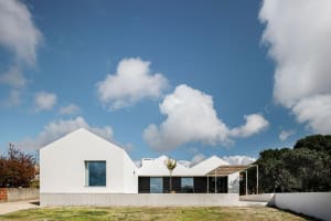 Modern minimalist house with white exterior and concrete accents, set against a blue sky with scattered clouds.