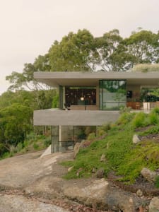 A modern minimalist cabin built into a hillside with concrete exterior and large windows.