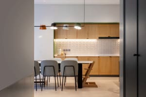 A modern, minimalist residential kitchen featuring commercial-grade lighting, wooden cabinets, and a white tile backsplash.