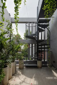 A modern interior space featuring a black metal staircase surrounded by potted plants and greenery.