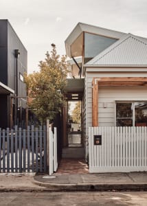 Modern house with wooden and metallic accents, featuring a white picket fence and a corrugated metal roof.