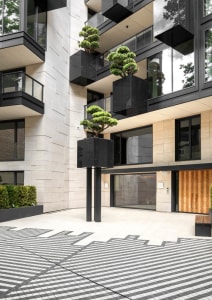 Modern residential building with concrete and black glass elements, featuring a geometric patio design and potted bonsai tree