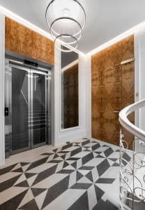 A modern elevator hall with metallic finishes, glass doors, and wooden accents.