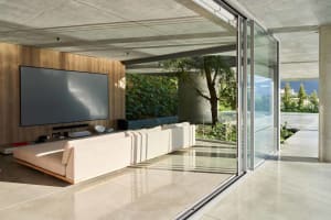 Contemporary living room with concrete walls and glass sliding doors overlooking a garden.