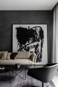 A modern living room featuring a beige sofa with decorative pillows, black tables, and a large black and white abstract paint
