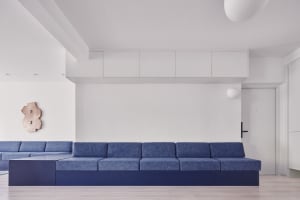 A modern minimalist living room featuring a blue sofa with a dark blue base and a rectangular metallic wall ornament.