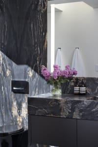 An industrial bathroom with black marble walls and a black marble countertop, featuring purple flowers in a vase and a black 