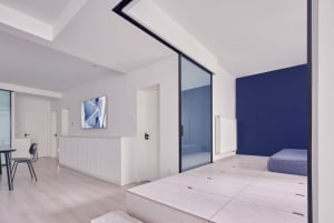Modern minimalist living space with white walls and wooden floor, featuring a sliding glass door and blue storage compartment