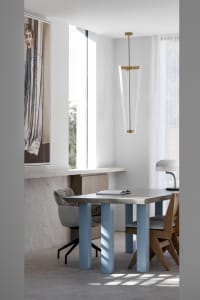 A minimalist home office featuring a metallic desk with blue accent columns, a sleek pendant light, and a large window with a