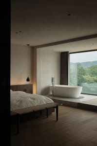 Modern minimalist bedroom featuring a concrete floor and a bathtub with a view of the mountains through a large window.