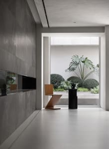 A modern lobby interior with a concrete floor, minimalist furniture, and a view of a green courtyard.
