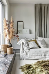 A minimalist bedroom featuring bed with textured white sheets and pillows, grey curtains, and a marble coffee table with deco