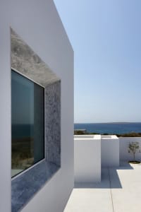 A minimalist white wall with a glass window overlooking the ocean.