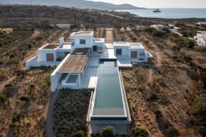 Aerial view of a modern house with a concrete pool surrounded by shrubbery and bushes. The house features minimalist architec