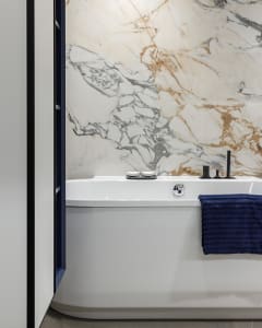 Modern minimalist bathroom featuring white marble walls and a white bathtub with blue towels.