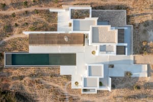 An aerial view of a minimalist house with a white exterior and concrete structural elements, featuring a long pool and open s