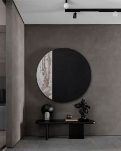 A minimalist entrance lobby featuring a metal table with various decorative items and a large circular artwork with a black a