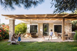 A modern farmhouse-style residential exterior with a wooden pergola and a family playing on the patio