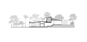 Modern house with concrete exterior and large windows against a tree-lined background.