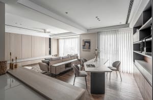 Modern minimalist living room with light wood furniture, gray sofa, and large windows with vertical blinds.