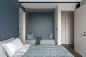 A minimalist bedroom featuring a comfortable seating nook with textured soft furnishings, including a grey bedspread and cush