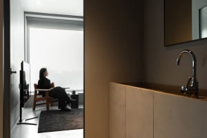A minimalist home office setup with a wood chair and table, framed by a large window.