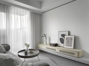 Neutral-toned minimalist living room with white curtains, round coffee table, and abstract artwork on the wall.