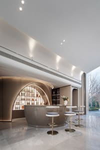 A modern bar interior with sleek, curved metal counters and glass shelves filled with bottles.