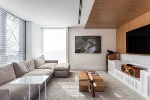A modern living room with concrete flooring, a beige sectional sofa, and a wooden TV stand with a flat-screen TV.