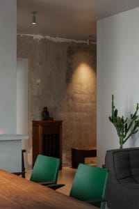 A modern living space featuring a concrete wall and green chairs around a wooden table.