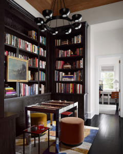A modern bookshelf library with dark hardwood flooring and a chandelier.