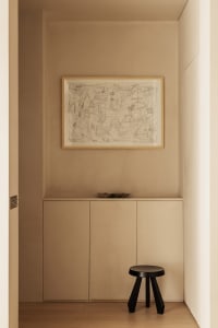 A minimalist entryway featuring neutral-toned cabinets and a black stool.