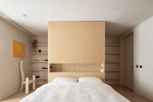 A minimalist bedroom with a wooden wall, white bedding, and floating shelves.