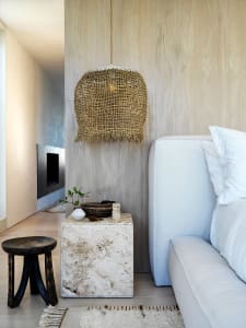 A textured lamp shade hanging above a white sofa, placed on a concrete side table with various decorative items such as a whi