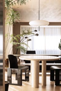 A modern dining room featuring a marble table and black chairs, illuminated by natural light.