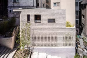 A minimalist building featuring a white brick facade with large glass windows and a green roof garden.