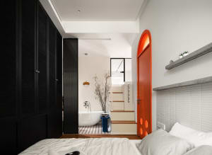 A minimalist bedroom featuring white walls, a black wardrobe, and an orange door.