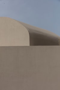 A minimalist sand hill with smooth, curved surfaces under a clear blue sky.