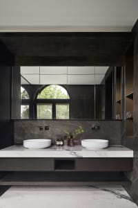 A modern bathroom with a marble countertop and vanity, featuring a large mirror and a window with green trees outside.