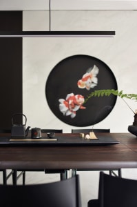 Modern dining room with minimalist black and wood furniture, a large circular art piece depicting fish, and an incense stick 