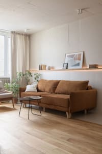 A modern living room featuring a brown sofa, wood panels, and green plants, with a picture on the wall.