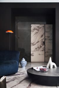 A modern living room featuring a dark marble coffee table with a bowl of fruit, an abstract white sculpture, and a blue uphol