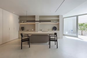 A modern minimalist office with a concrete desk, black chairs, and a sleek, white storage unit with built-in shelves.