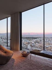 Modern living room featuring large windows overlooking a rocky landscape at sunset.
