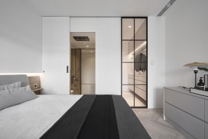 Modern minimalist bedroom with white walls, a bed, and a sliding glass door leading to a closet.