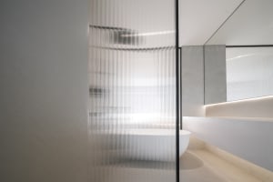 Modern minimalist bathroom featuring translucent glass walls, a freestanding white bathtub, concrete walls, and a sleek light