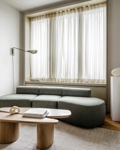 Modern living room with a green sofa, wooden coffee table, and large window with sheer curtains.